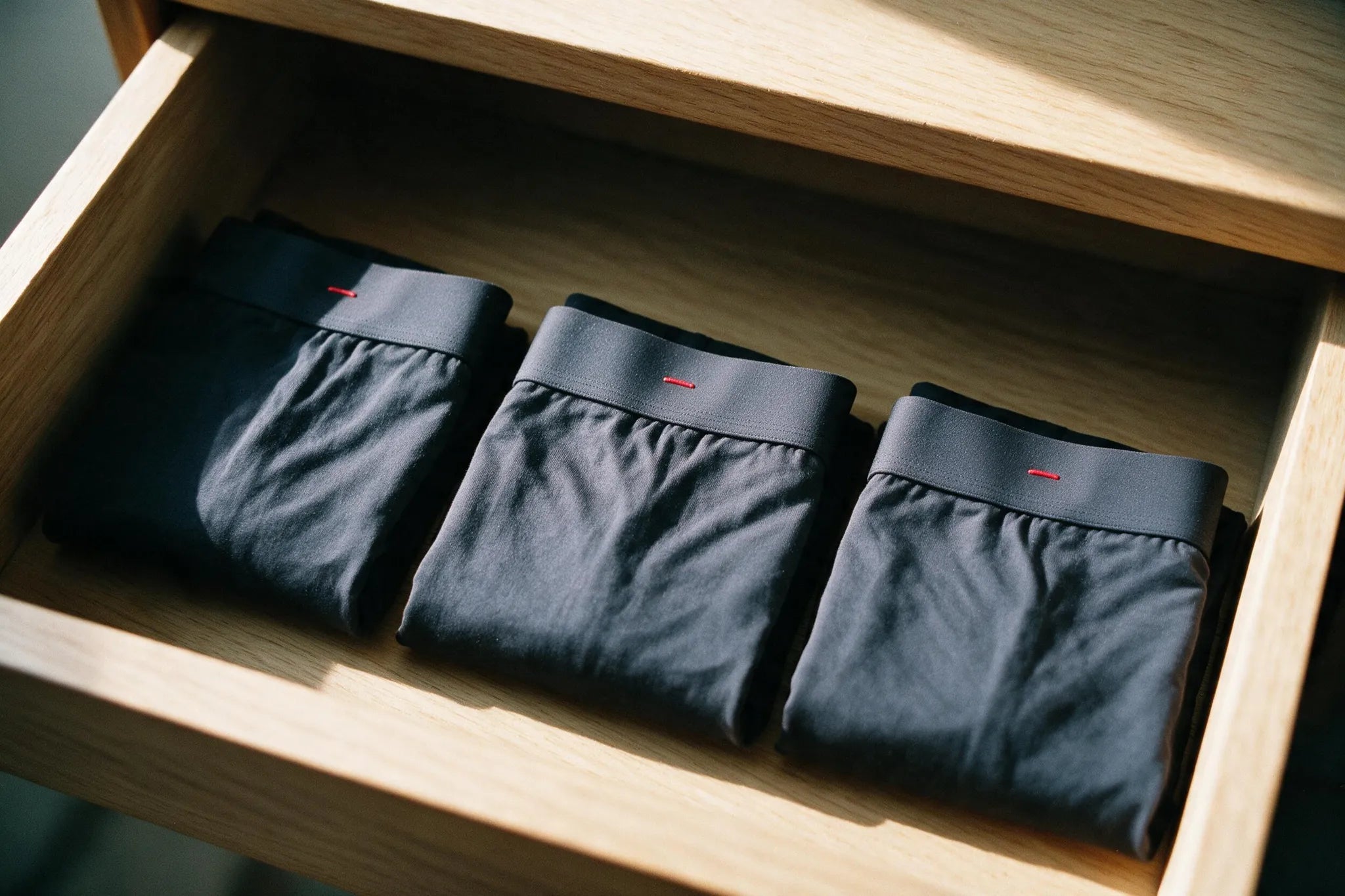 A walnut drawer of folded ātem boxer-briefs in black and white